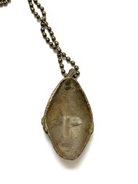 back side of a bronze pendant necklace featuring an abstract face design, hanging from a ball chain, displayed on a white background.