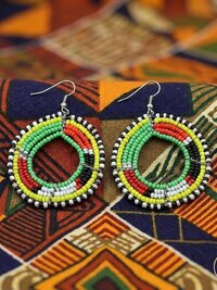 A pair of colorful beaded hoop earrings with green, yellow, white, red, and black beads, displayed on vibrant geometric-patterned fabric.