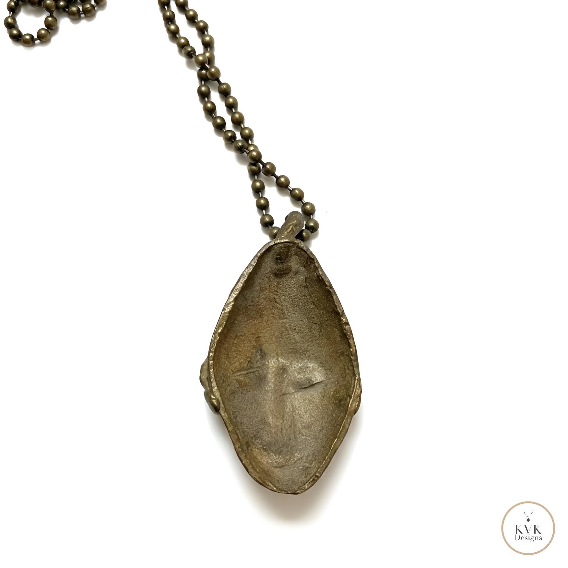 back side of a bronze pendant necklace featuring an abstract face design, hanging from a ball chain, displayed on a white background.